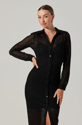 A woman is wearing a long black dress made of a sheer, textured, see-through fabric. The dress features a button-up front with small black buttons, a classic collar, and long sleeves. The fabric appears lightweight with a perforated pattern, giving it a delicate and breathable appearance.
